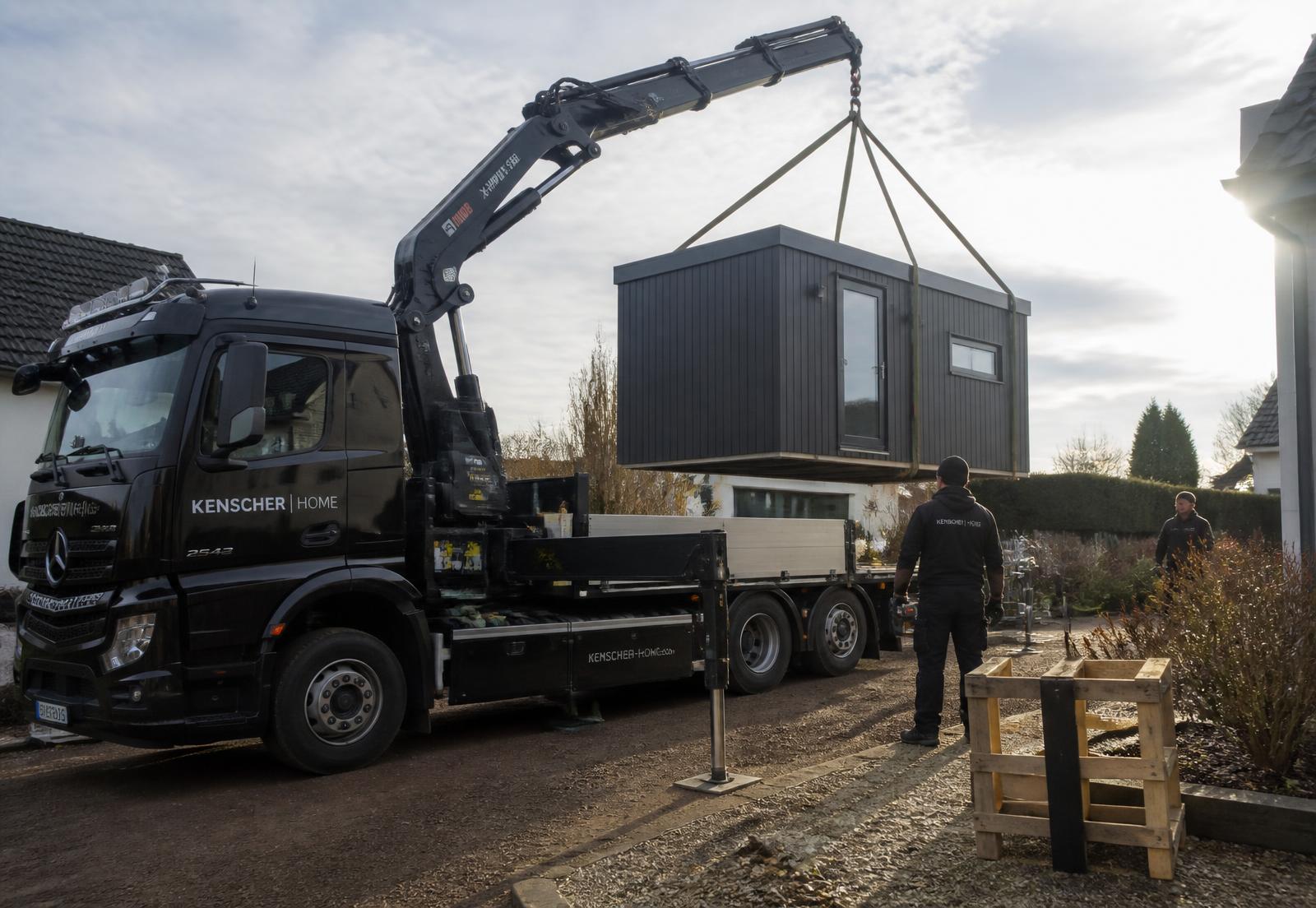 Kranwagen setzt eine schwarze Modulsauna in einen deutschen Garten
